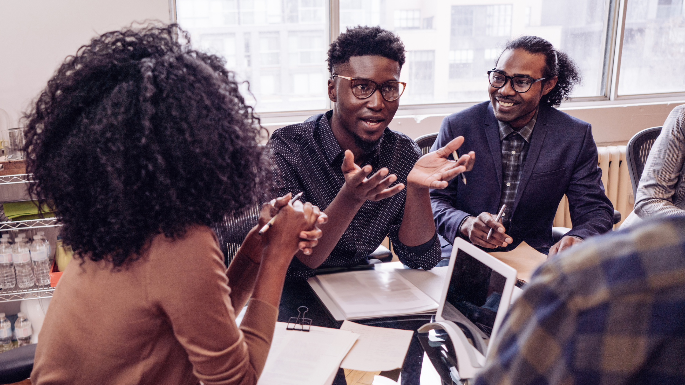 Three business professionals sit at table with notes and an open laptop discussing an issue that is related to the business matter at hand, potentially discussing leadership development strategies.