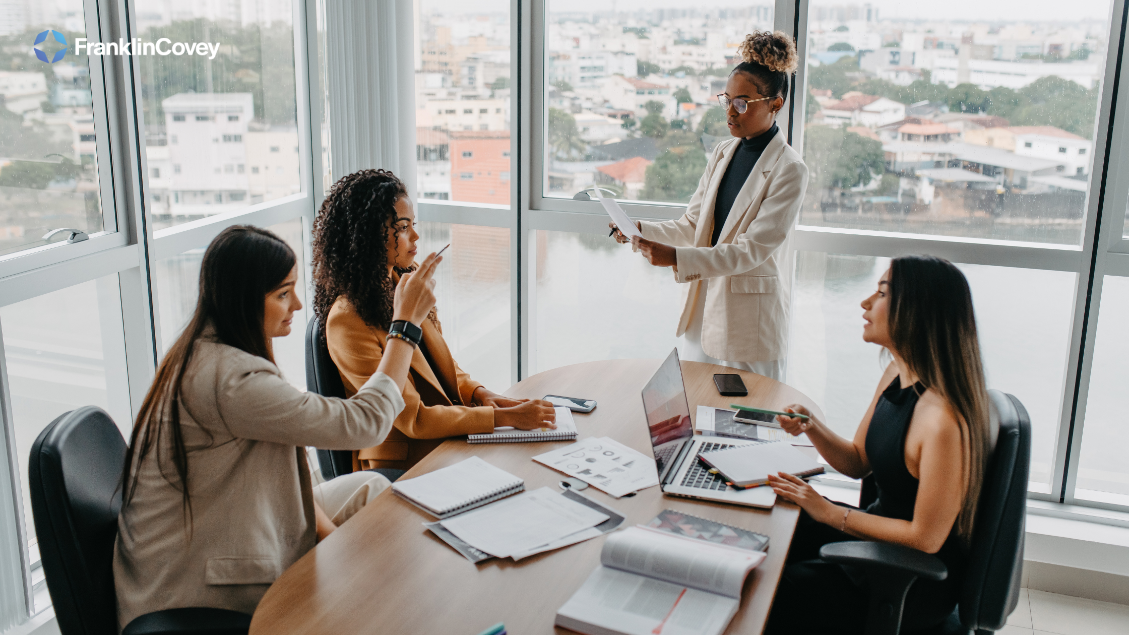 Three women who are business professionals sit round a table discussing an issue that is related to the business matter at hand.